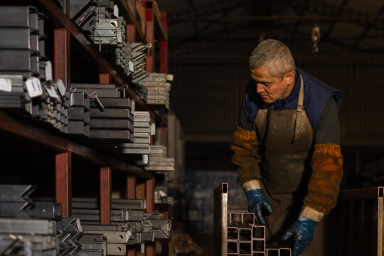 Industrial worker organizing metal materials on cart beside storage rack