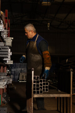 Industrial worker loading metal pieces onto cart beside storage rack