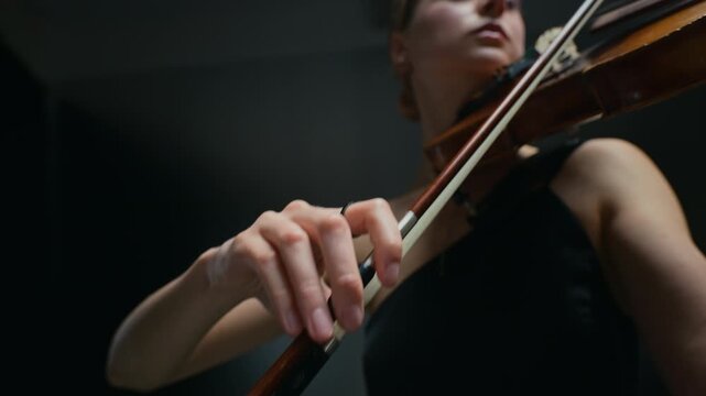 Young adult Caucasian woman playing violin, moving bow across strings in close-up low angle shot. Clip is ideal for classical music promotions, artistic documentaries, or cultural event ads