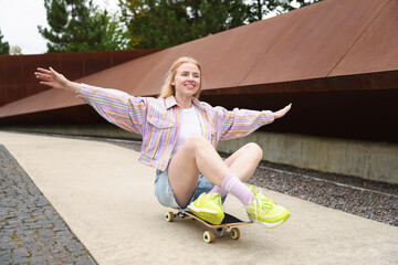 Happy woman riding skateboard while sitting outdoors © New Africa
