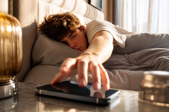 Teenager reaching for a smartphone immediately after waking, representing habitual screen checking and digital dependence.