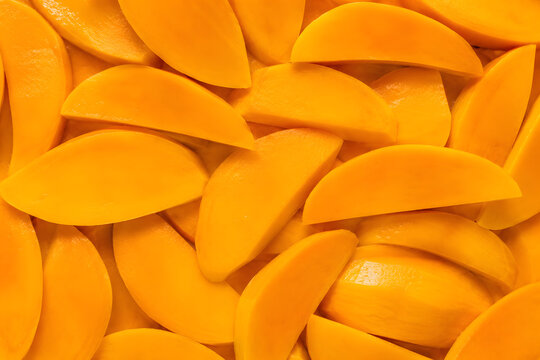 Bright orange mango slices in a full frame background texture pattern.