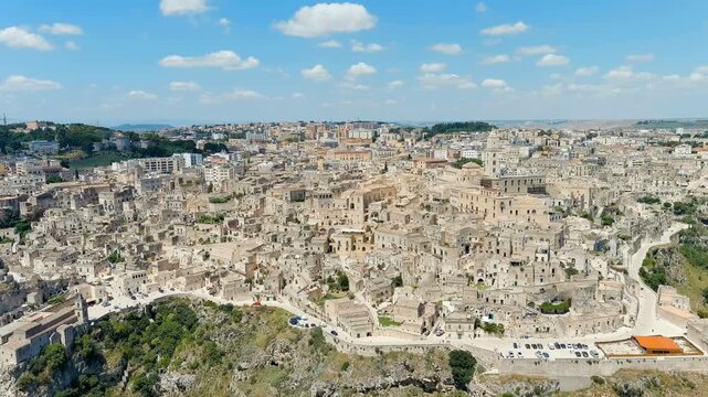 Matera, Italy. The ancient Sassi cave districts, a dense cluster of stone dwellings carved into limestone cliffs, seen in a sweeping Drone footage under a bright summer sky. Drone footage, Point of i