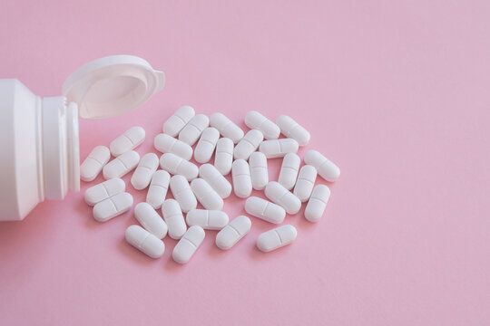 White tabletts or pills on the pink background with place for text.
