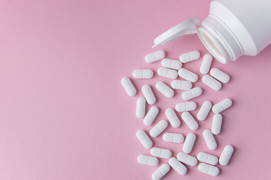 White tabletts or pills on the pink background with place for text.