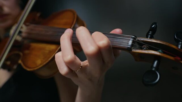 Caucasian young adult woman playing violin, fingers pressing strings on fingerboard in extreme close-up. Clip is perfect for music school promos or classical concert advertisements