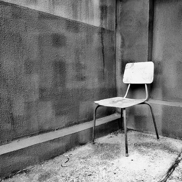 Empty old vintage school chair standing in the corner of a rough concrete wall. Black and white conceptual minimalist shot