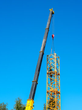 Tower Crane Assembly with Mobile Crane Lifting Mast Section and Worker at Height on Construction Site