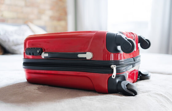 Red Carry-On Suitcase Sitting On A Bed As Sunlight Streams Into The Hotel Room