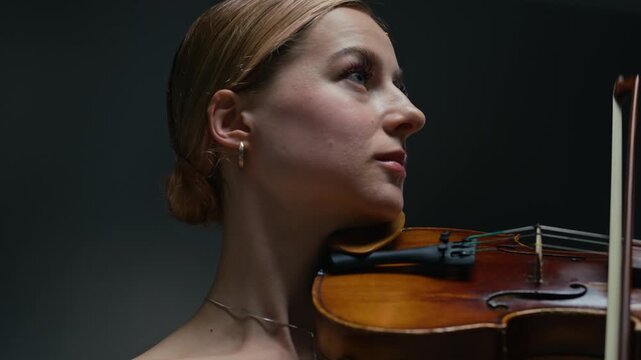 Young adult Caucasian woman playing violin with deep concentration against dark background. Perfect for classical music school advertisements, talent showcases, or online tutoring platforms