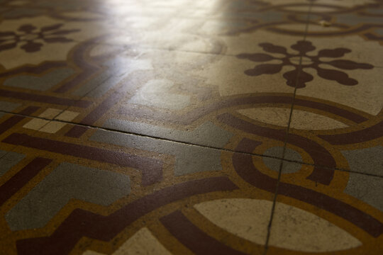 Low-angle close-up: vintage hydraulic floor. Warm light reflects on worn tiles, highlighting intricate geometric, floral patterns. 