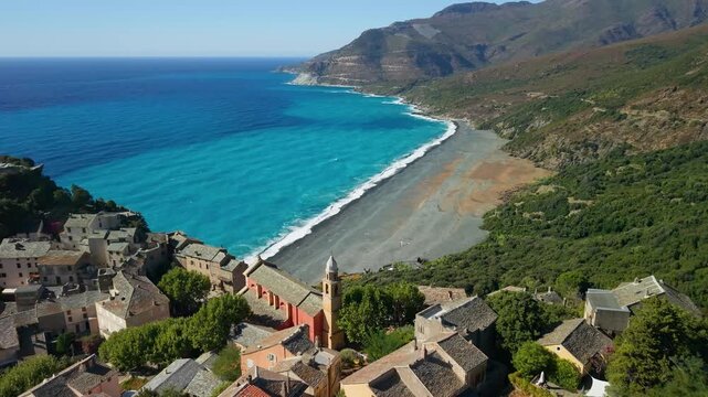 Nonza village aerial drone backward reveal shot with Genoese tower and chapel in Corsica France. Perched cliffside houses black beach 4K 