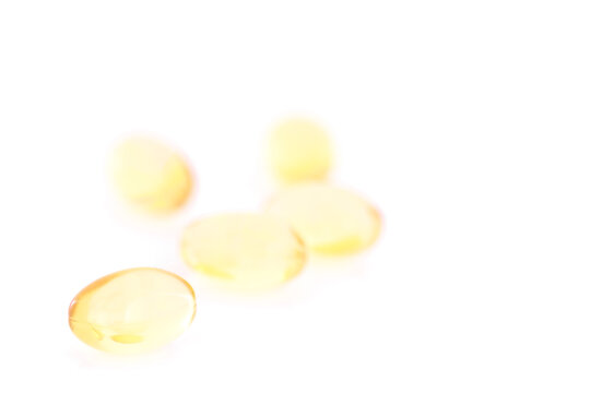Close-up of several fish oil Omega-3 gel capsules on white background. Yellow transparent capsules viewed from the front. Shallow depth of field, focused on the foreground. Copy space.