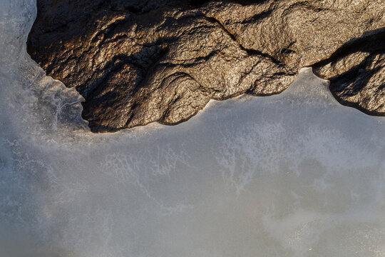 Close-up of a glistening rock and ice on a frozen lake in Finland in winter, viewed from above. Abstract full frame textured wintry background. Copy space, top view.