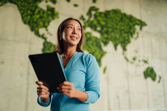 Asian businesswoman holding digital tablet, envisioning global business strategy, sustainability, and technological innovation