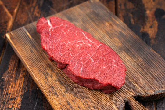 Raw beef knuckle sirloin tip on wooden cutting board with butcher cleaver, thyme and red peppercorns. Fresh lean red meat on rustic wooden background with copy space.