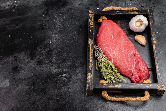 Fresh raw beef inside round topside with thyme herb and garlic on wooden tray. Lean butcher cut meat on dark background, top view.
