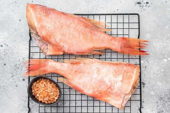 Cut ocean red perch fish on metal rack with thyme. Raw marine seafood ingredient ready for cooking.