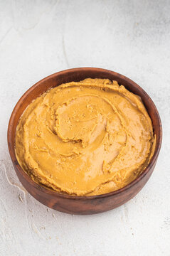 Peanut butter paste in wooden bowl with spoon on round cutting board. Creamy nut spread made from roasted peanuts with copy space.