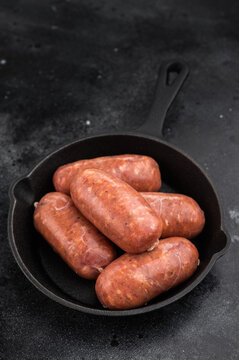Raw butcher style pork sausages in cast iron pan on dark background, fresh uncooked sausage links ready for grilling or frying.