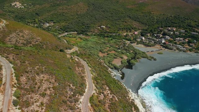 Cap Corse winding coastal road Corsica 4K drone view. Serpentine mountain road trip leading to Albo black beach and turquoise Mediterranean sea. Scenic driving route travel b roll stock footage