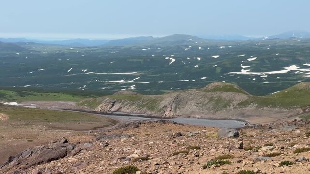 Panoramic view from Opasny Canyon reveals vast volcanic highlands with scattered snowfields in Kamchatka. Remote wilderness, volcanic landscape, geology, exploration, adventure tourism