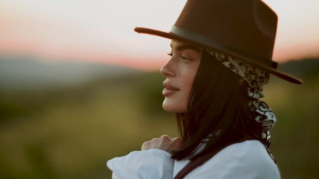 Young woman relaxing outdoors wearing a brown fedora hat during a peaceful golden sunset period