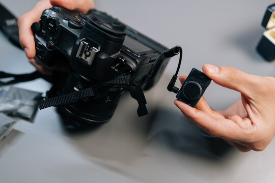 Close-up cropped shot of content creator setting up and synchronizing wireless lapel microphone system, connecting receiver to digital camera for professional audio recording.