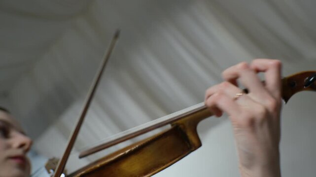 Caucasian young adult female violinist playing classical music, closeup on hand pressing strings on fingerboard. Footage is ideal for music school advertisements or classical concert promotions