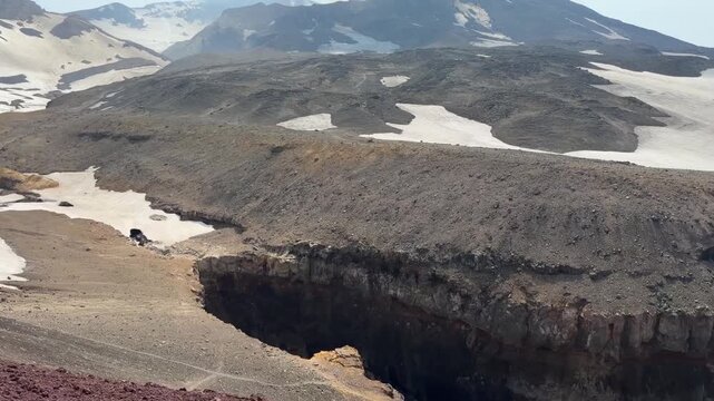 Opasny Canyon cuts through rugged volcanic terrain with snowfields near Gorely Volcano in Kamchatka. Volcanic geology, dramatic landscape, wilderness exploration, adventure tourism