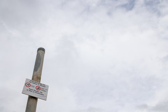 Welsh dog fouling fixed penalty notice mounted on a metal post at Penrhyn Bay in Wales with bilingual council wording and cloudy sky above the public coastal area and local streetscape
