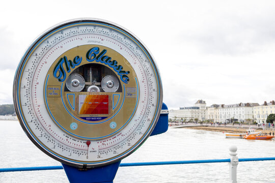 Traditional seaside weighing machine called The Classic on Llandudno seafront in North Wales with an imperial and metric dial overlooking the bay and Victorian waterfront buildings