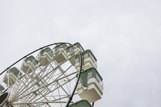 Traditional Ferris wheel at Llandudno in North Wales viewed from below with white metal framework enclosed passenger gondolas and coloured lights rising against a pale cloudy sky