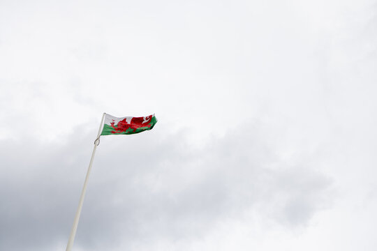 Welsh national flag flying from a tall flagpole in Llandudno North Wales with the red dragon clearly visible against an expansive cloudy sky above the coastal Welsh resort town