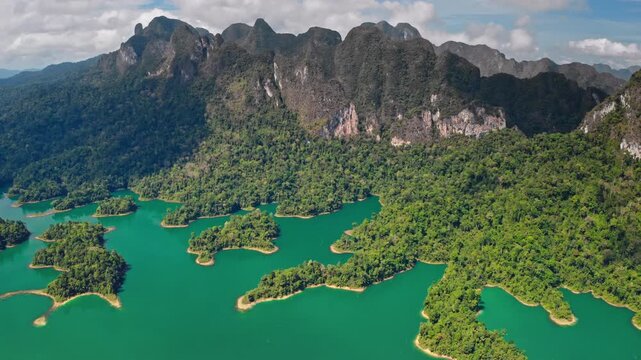 Dramatic limestone karst mountains rising above the emerald green waters of Cheow Lan Lake dotted with lush jungle islands. Travel and explore Khao Sok National Park, Thailand. Aerial view drone shot