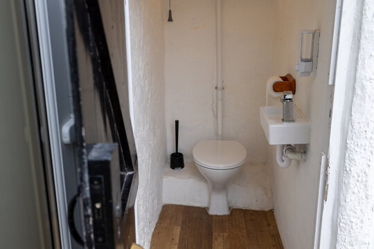 Compact outside toilet at Penrhyn Bay North Wales viewed through the doorway with white WC small hand basin exposed plumbing wooden flooring toilet brush and dispensers