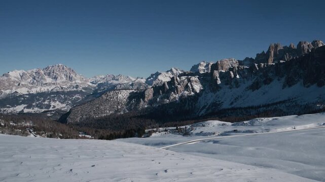 Snowy mountain range under a clear blue sky. Smooth, white slopes stretch into the distance. Rugged peaks define the horizon's edge. Ideal for outdoor adventures and natural beauty content
