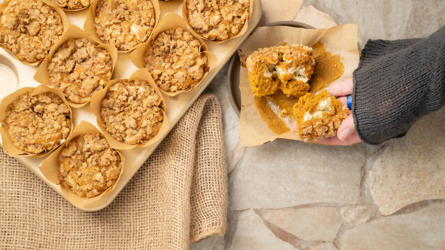 Hand holding an open, freshly baked pumpkin cream cheese muffin with streusel topping