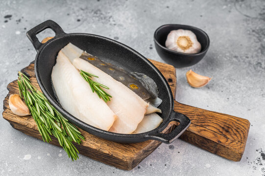 Raw fluke flatfish fillet pieces with rosemary and garlic in iron pan on wooden board, fresh marine seafood ingredient with copy space