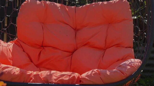 Bright orange hanging chair in backyard with green plants around it