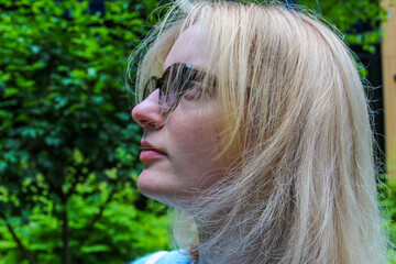 Warsaw, Poland, May 15, 2026. Profile portrait of blonde woman looking up outdoors against lush green foliage background. High quality photograph © ULYANA_1995