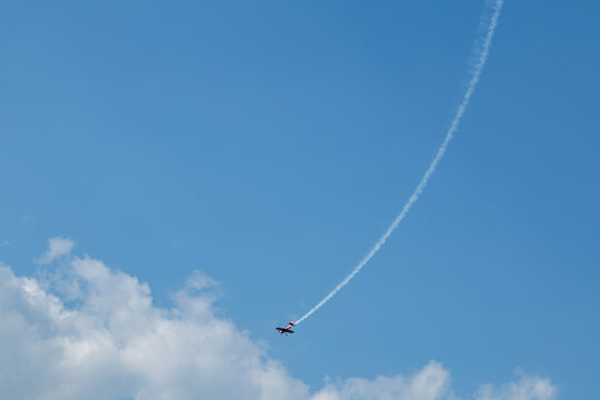 Airshow performance of a red aerobatic plane with dramatic contrail streaks in scenic sky