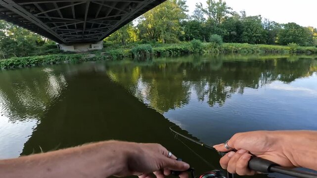 POV angler spin fishing under a concrete river bridge. Reeling in artificial lure targeting predatory asp (Leuciscus aspius) in the city.