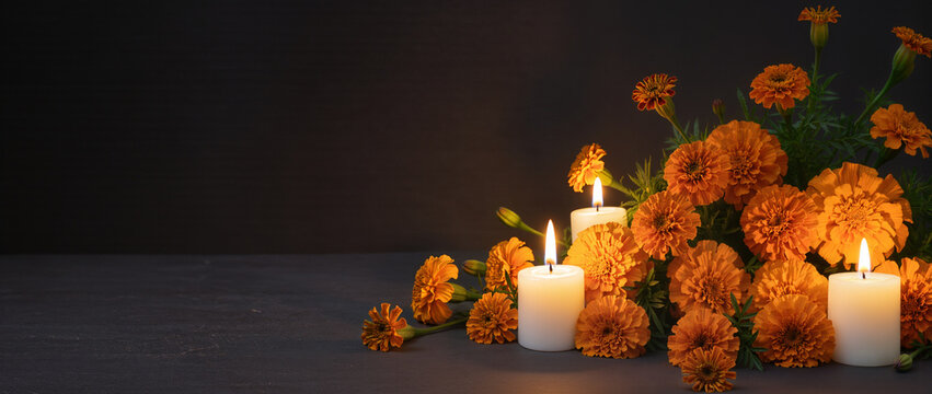 Traditional Day of the Dead altar with burning white candles and orange marigolds. Dia de los Muertos ofrenda on dark stone background. Copy space