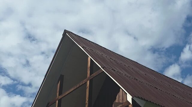 Roof of a house under a clear sky with clouds in the background