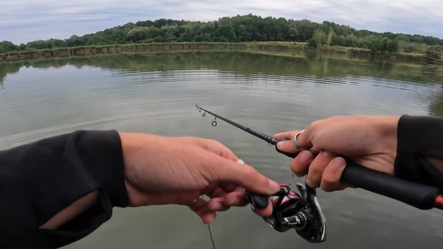 POV fisherman reeling artificial bait on a peaceful calm lake surrounded by green forest. Catching predatory asp (Leuciscus aspius).