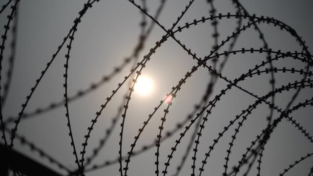 The sun is peeking over the barbed-wire fence.
