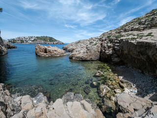 Fototapeta premium Rocky cove with clear turquoise water and distant town under a blue sky