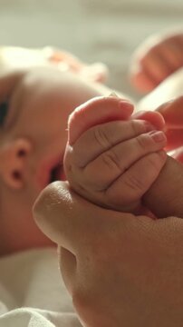 Vertical video of newborn baby hand squeezing mother finger close up view, parent stroking tiny palm, infant nutrition and wellness concept. Maternal emotional bonding. Newborn skin and pediatric care