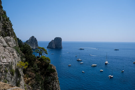 Scenic Coastline View of Faraglioni Rock Formations in Capri, Italy. A panoramic, high-angle view of the iconic Faraglioni sea stacks towering over the deep blue waters of the Mediterranean Sea. The s